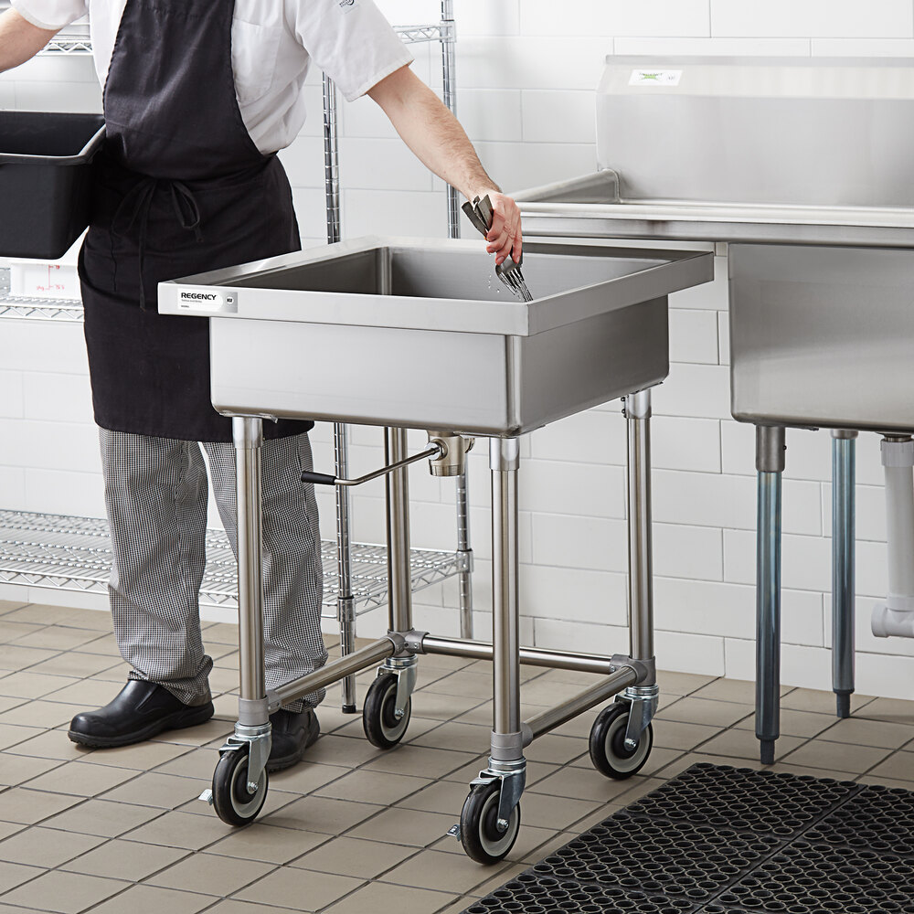 A stainless steel mobile soaking sink with four caster wheels is shown in a commercial kitchen setting, with a person placing utensils inside.
