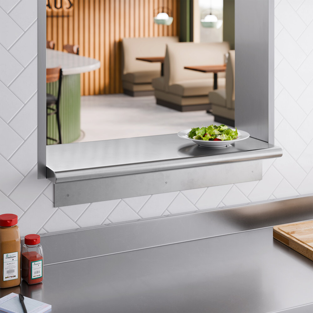 A stainless steel pass-through shelf mounted on a wall, with a plate of salad placed on top.