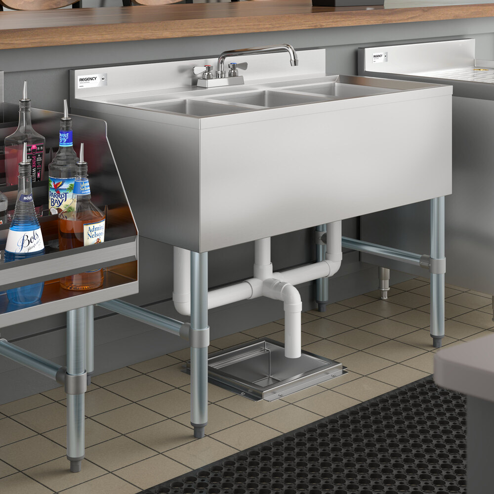 A stainless steel three-compartment sink with a faucet, installed under a countertop in a commercial setting.