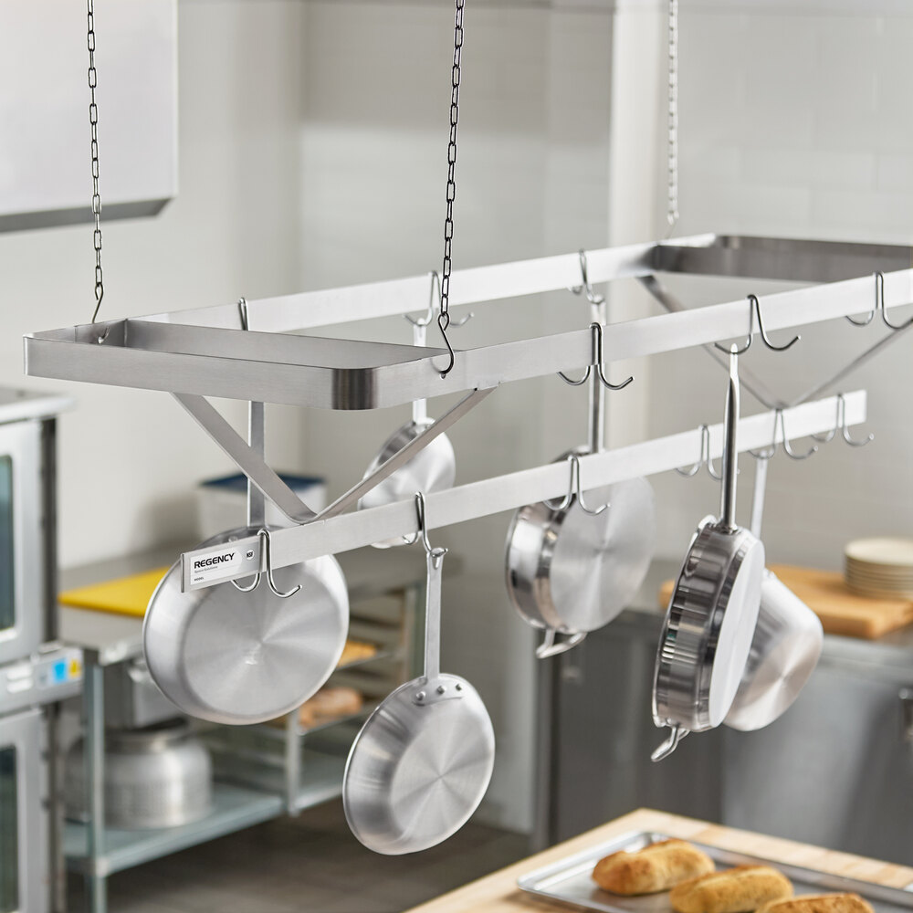 A stainless steel ceiling-mounted rack with several pots and pans hanging from hooks in a commercial kitchen setting.