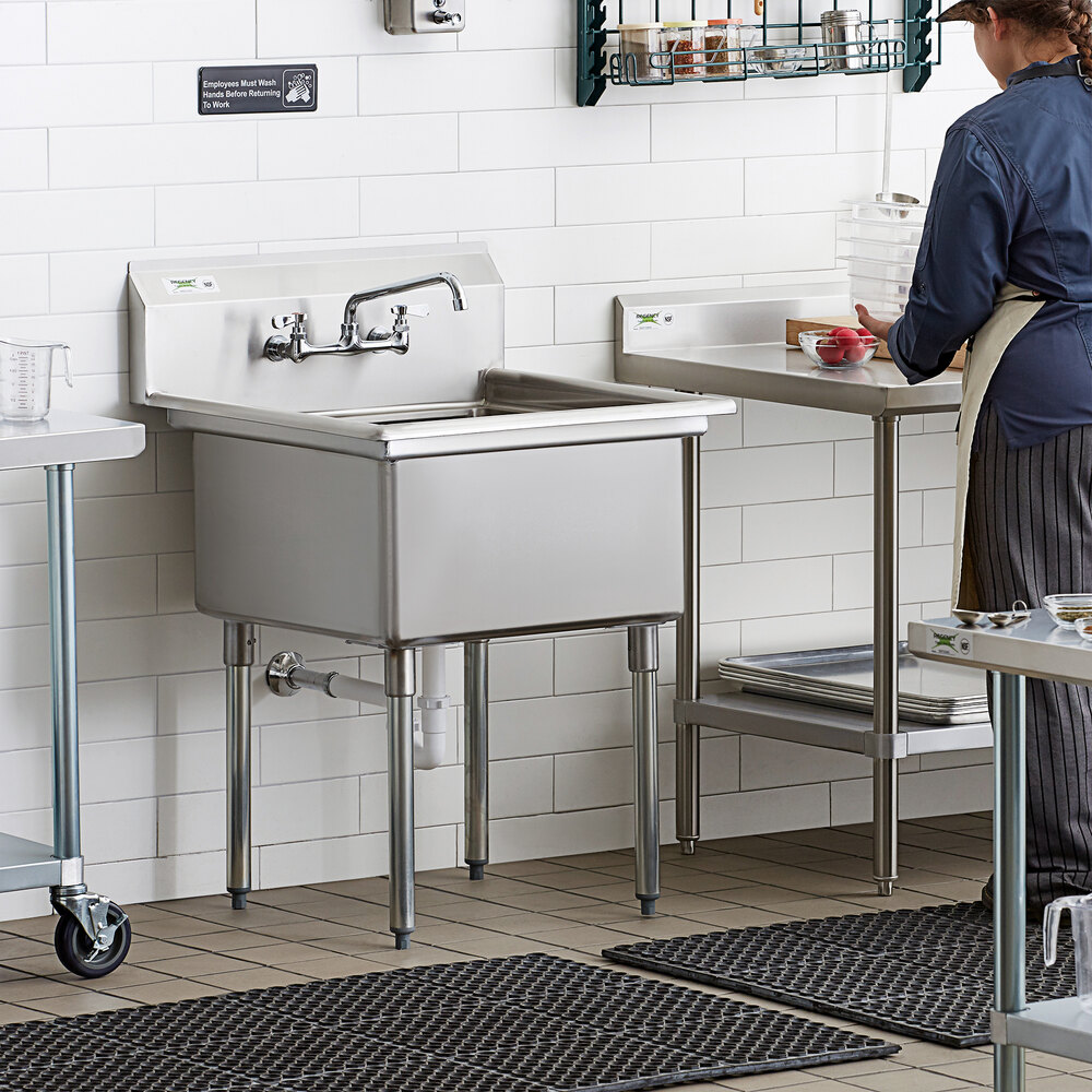 A woman washing dishes in a commercial kitchen using a Regency stainless steel 1 compartment sink.