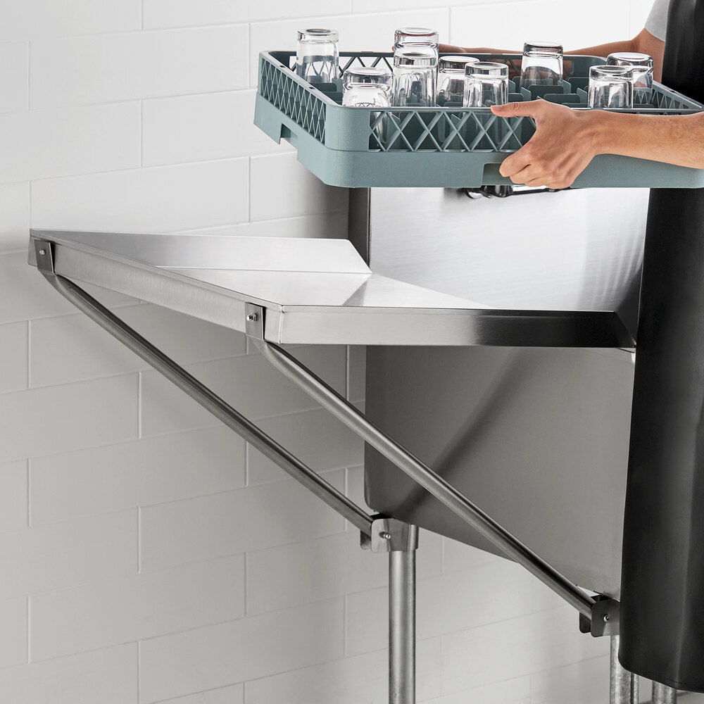 A person is placing a rack of glasses onto a stainless steel detachable drainboard mounted on a wall.