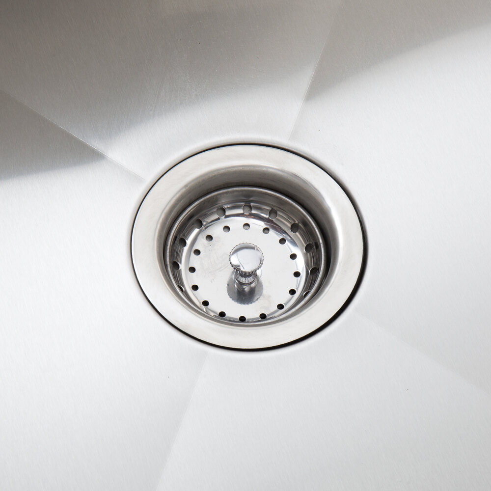 A stainless steel sink drain with a strainer basket in a commercial work table.