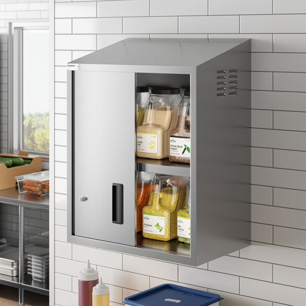 A stainless steel wall cabinet with sliding doors, mounted on a tiled wall and used for storing kitchen ingredients.