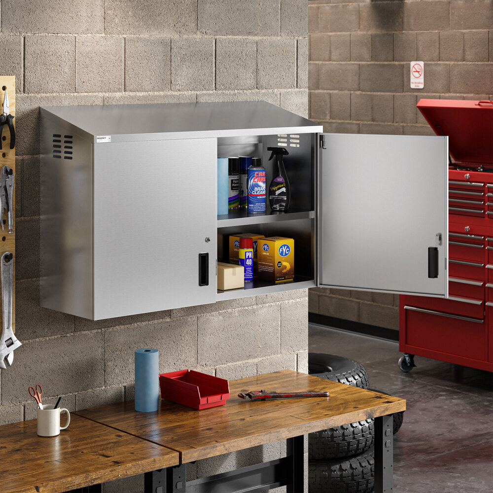 A stainless steel wall cabinet with hinged doors mounted above a workbench in a garage or workshop setting.
