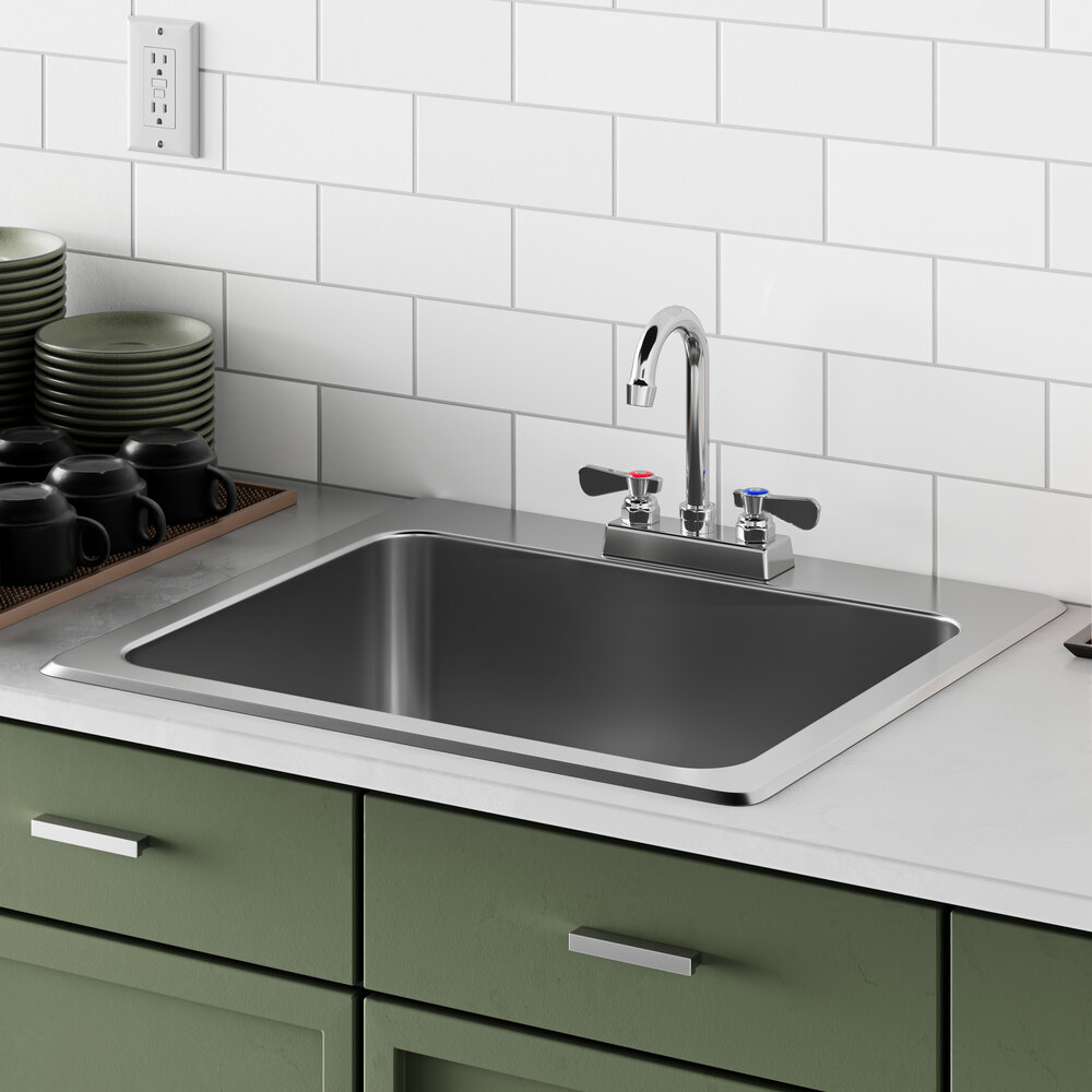A Regency stainless steel drop-in sink in a counter with green cabinets and countertops.