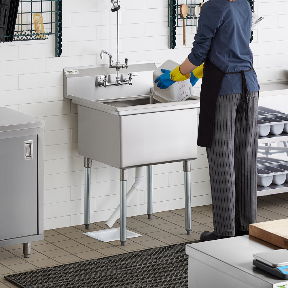A woman wearing gloves washing dishes in a Regency stainless steel commercial sink.