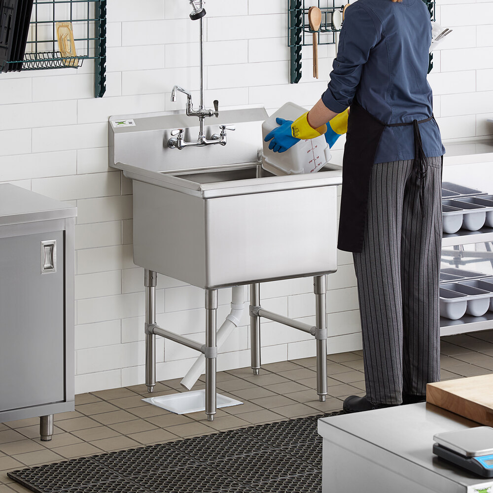 A woman wearing gloves washing dishes in a Regency stainless steel commercial sink.