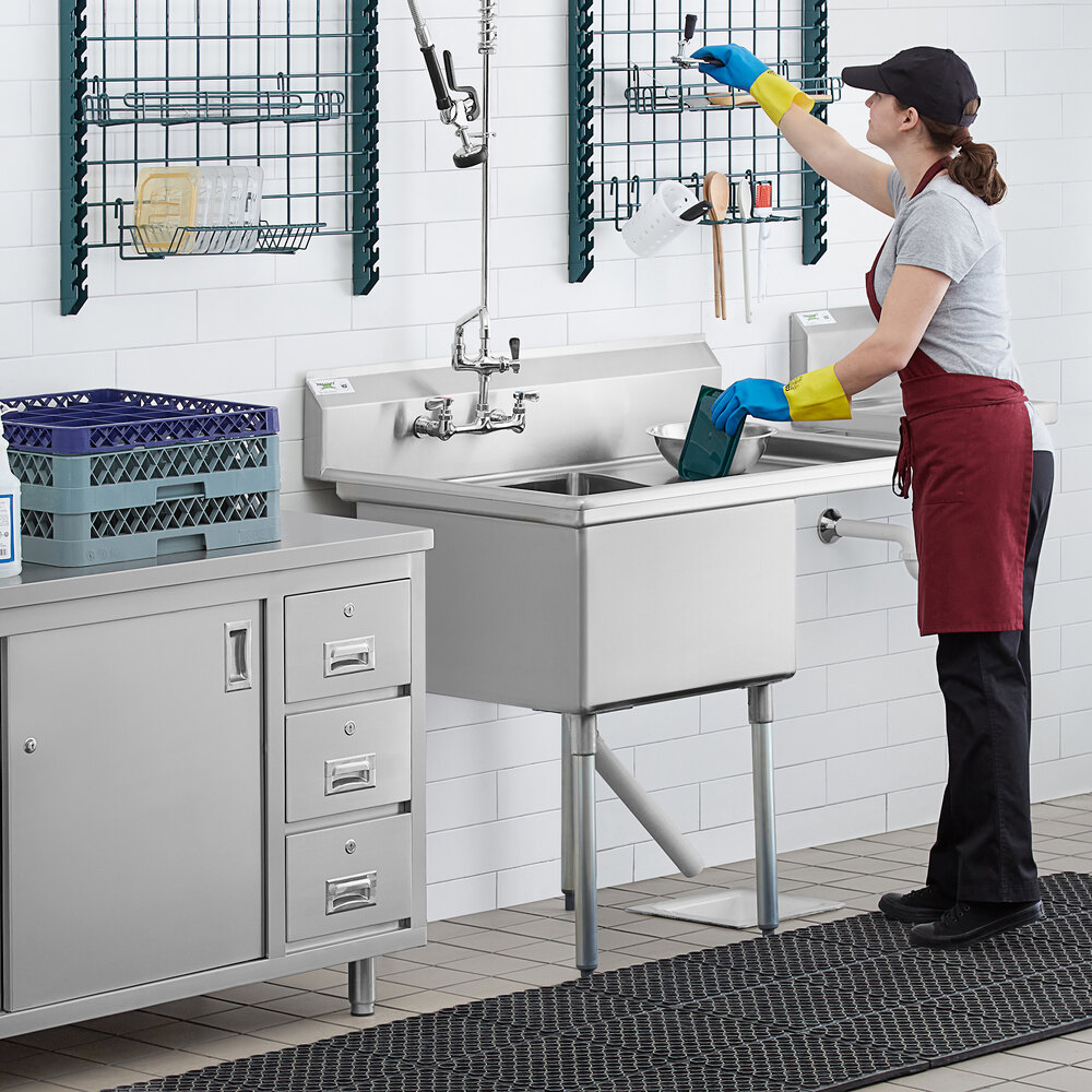 A woman wearing gloves cleaning a Regency stainless steel commercial sink.