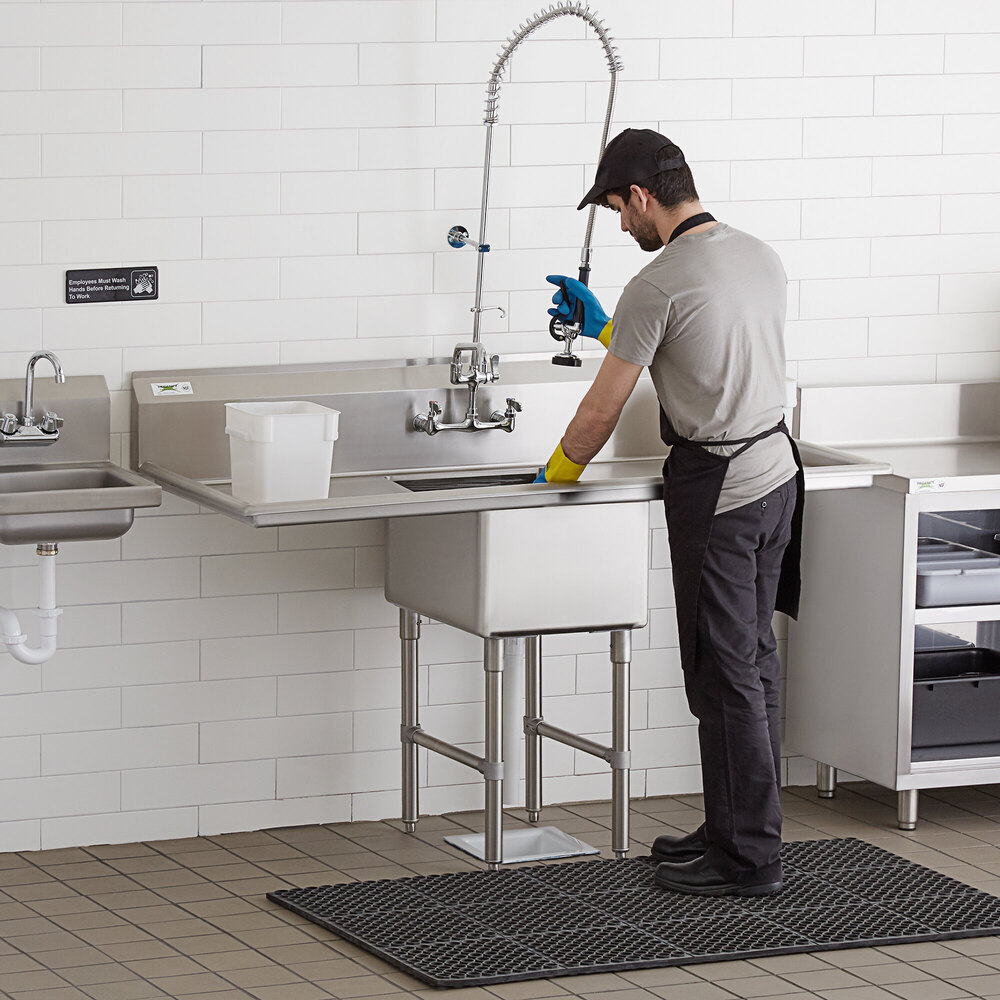 A man washing a Regency stainless steel commercial sink in a professional kitchen.