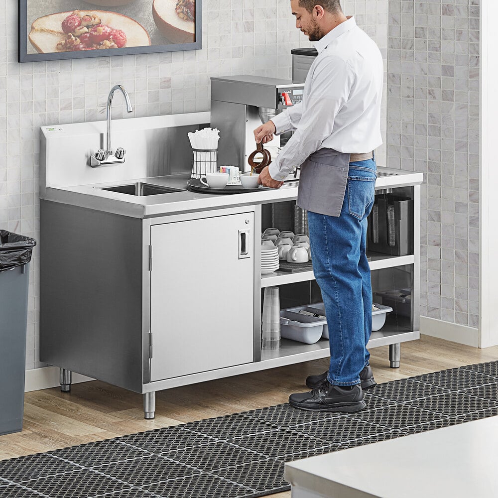 A man standing in a professional kitchen next to a Regency stainless steel beverage table with a sink.