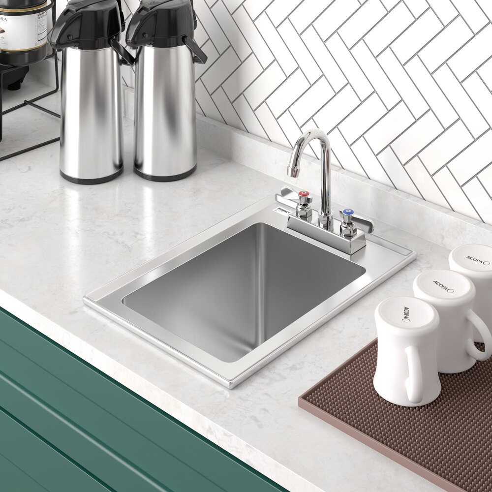 A stainless steel drop-in sink with a single compartment is installed in a white countertop, accompanied by a faucet with hot and cold handles, and surrounded by coffee dispensers and mugs.
