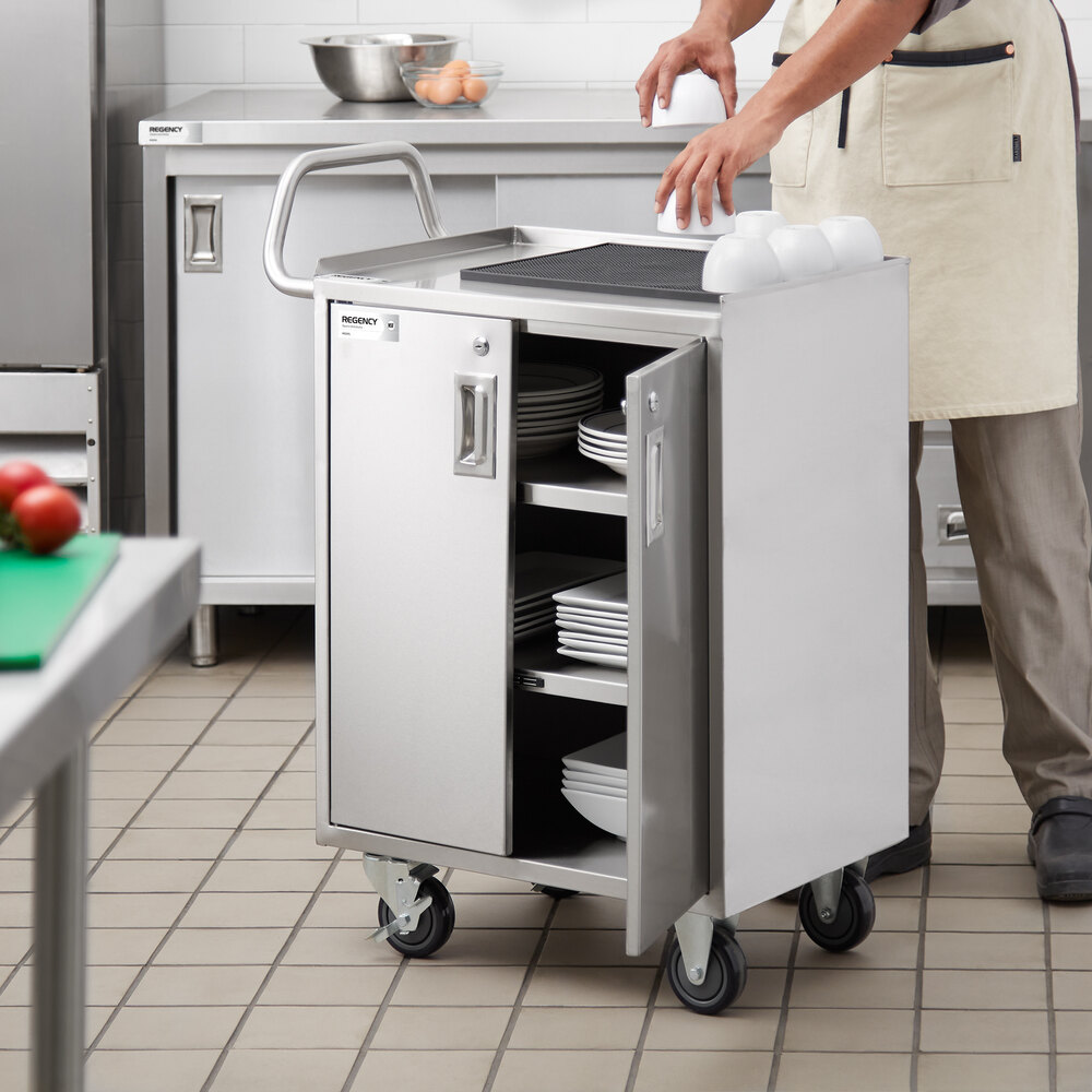 A stainless steel utility cart with four shelves, locking doors, and wheels, shown in a commercial kitchen setting with plates stored inside.