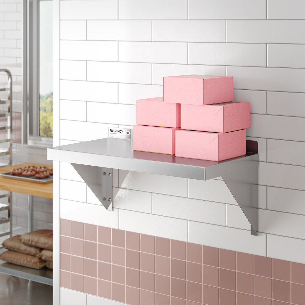 A stainless steel wall-mounted shelf holding several pink boxes.