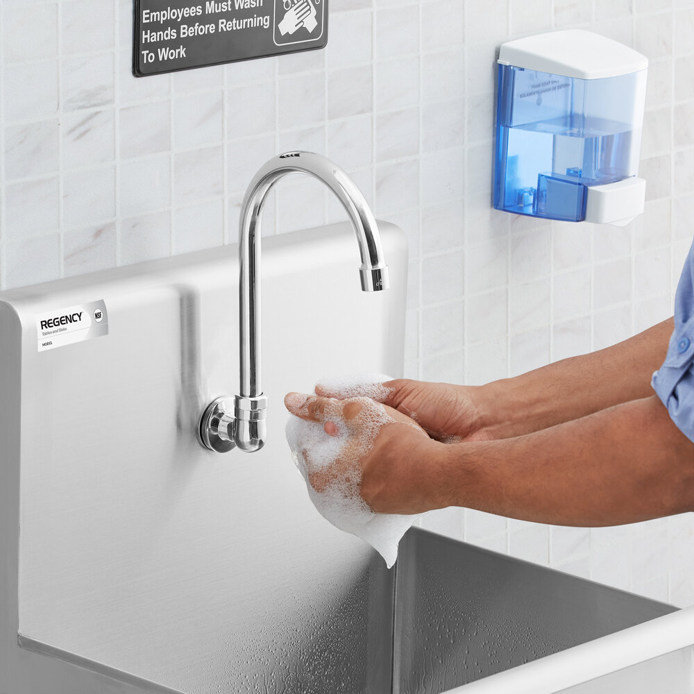 A person is washing their hands with soap at a stainless steel sink with a tall, curved faucet in a tiled setting.
