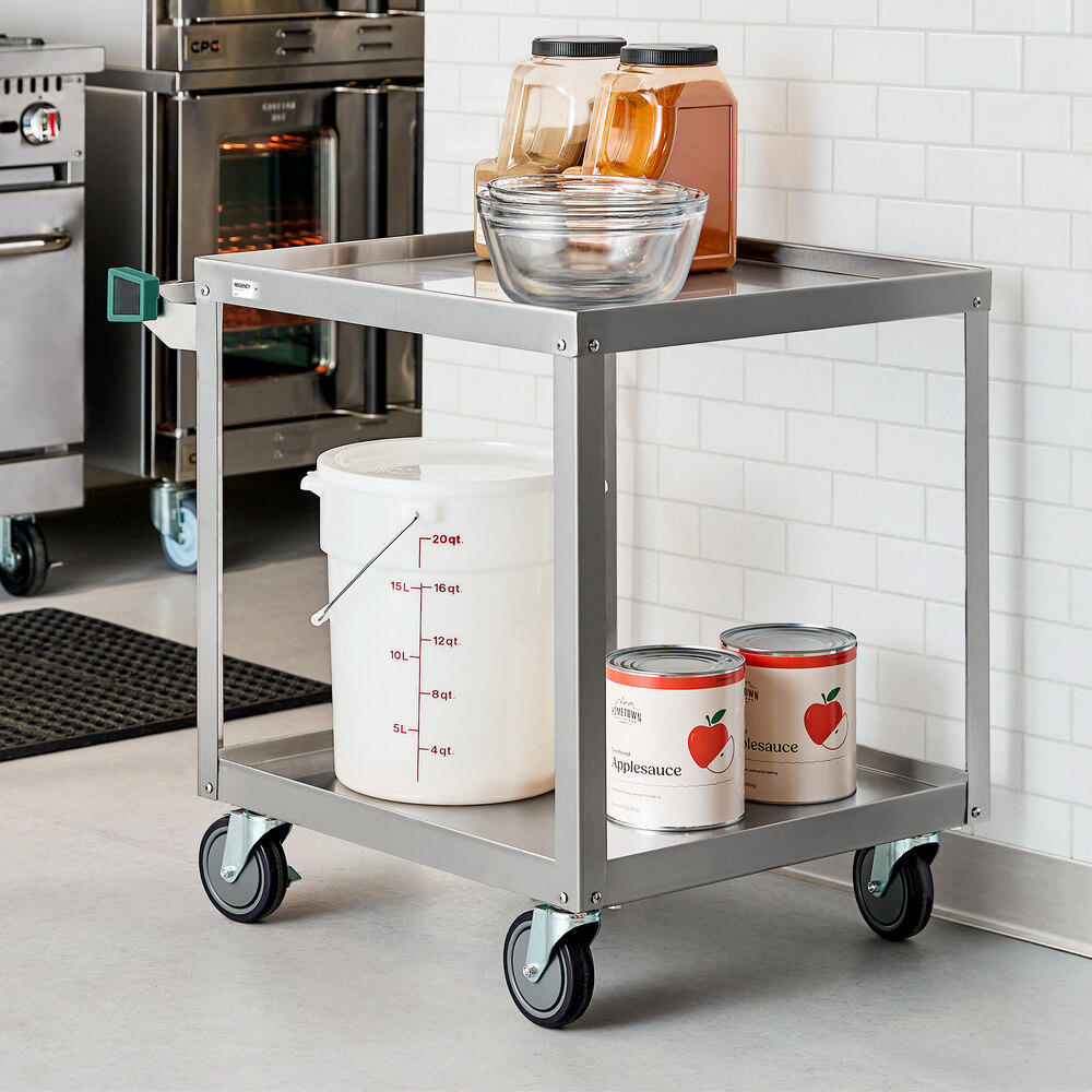 A stainless steel utility cart with two shelves, holding food containers, mixing bowls, and large cans, situated in a commercial kitchen setting.
