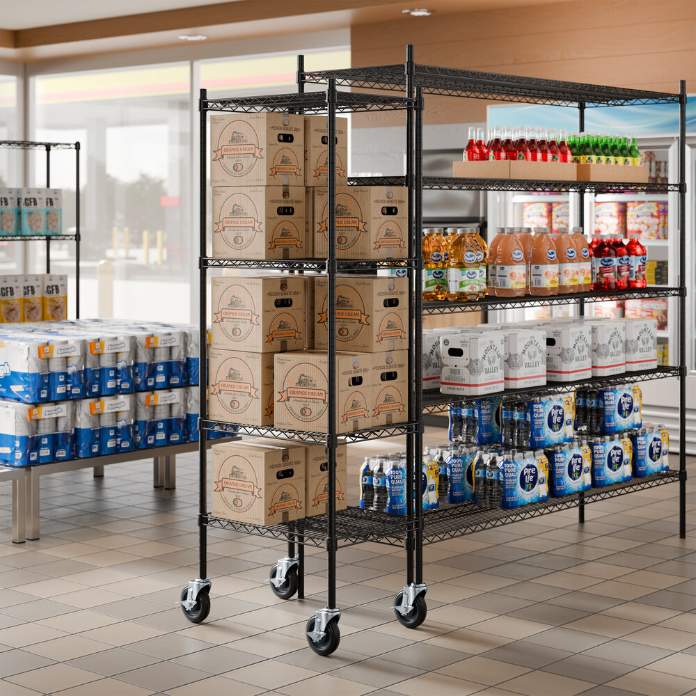 A black metal wire shelving unit on wheels with four shelves, stocked with boxes, bottled drinks, and other grocery items in a store setting.