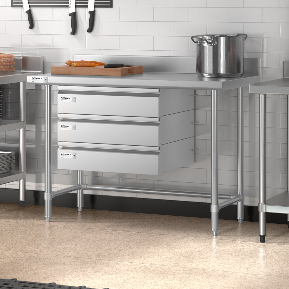 A stainless steel work table with three drawers, a 4-inch backsplash, and an open base, situated in a commercial kitchen setting.