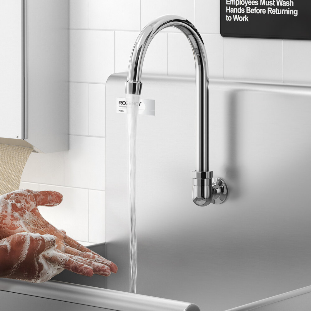 A person is washing their soapy hands under a tall, curved, wall-mounted faucet in a stainless steel sink.