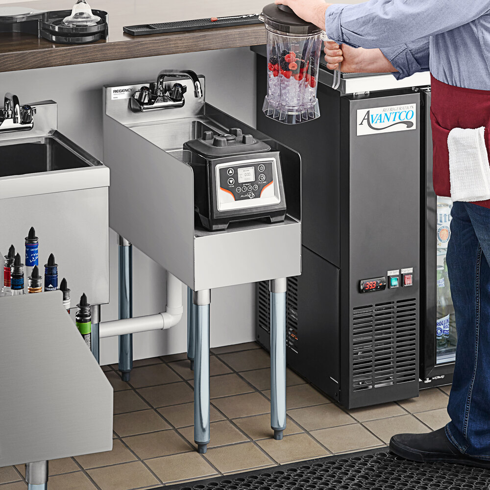 A stainless steel blender station with a dump sink and faucet, featuring a blender and a person holding a blender jar with ice and berries.