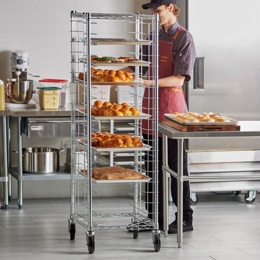 A tall, metal wire rack on wheels holds multiple trays of baked goods in a commercial kitchen setting.