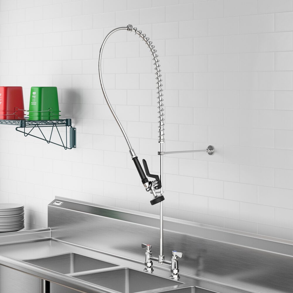 A commercial-style pre-rinse faucet with a long flexible hose and spray nozzle mounted above a stainless steel sink.