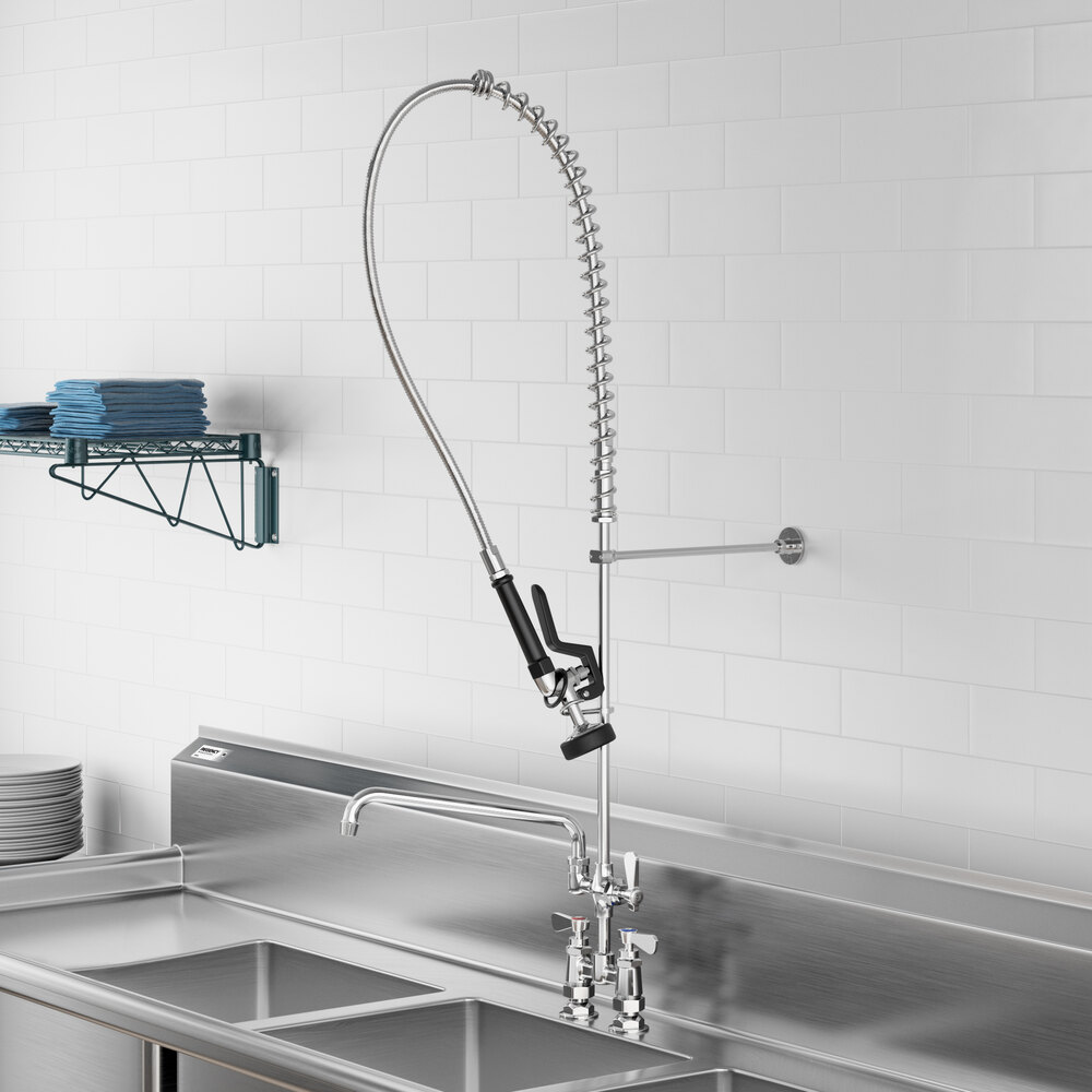 A commercial-style pre-rinse faucet with a flexible hose and spray nozzle mounted above a stainless steel sink, featuring an additional straight spout and dual handles.