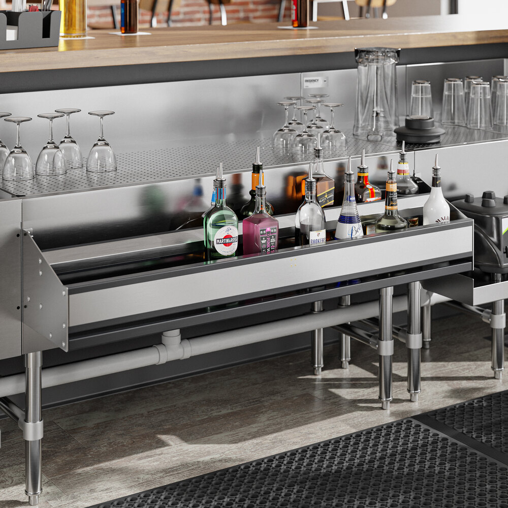 A stainless steel double-tier speed rail holding various liquor bottles beneath a bar counter, with glassware stored above.
