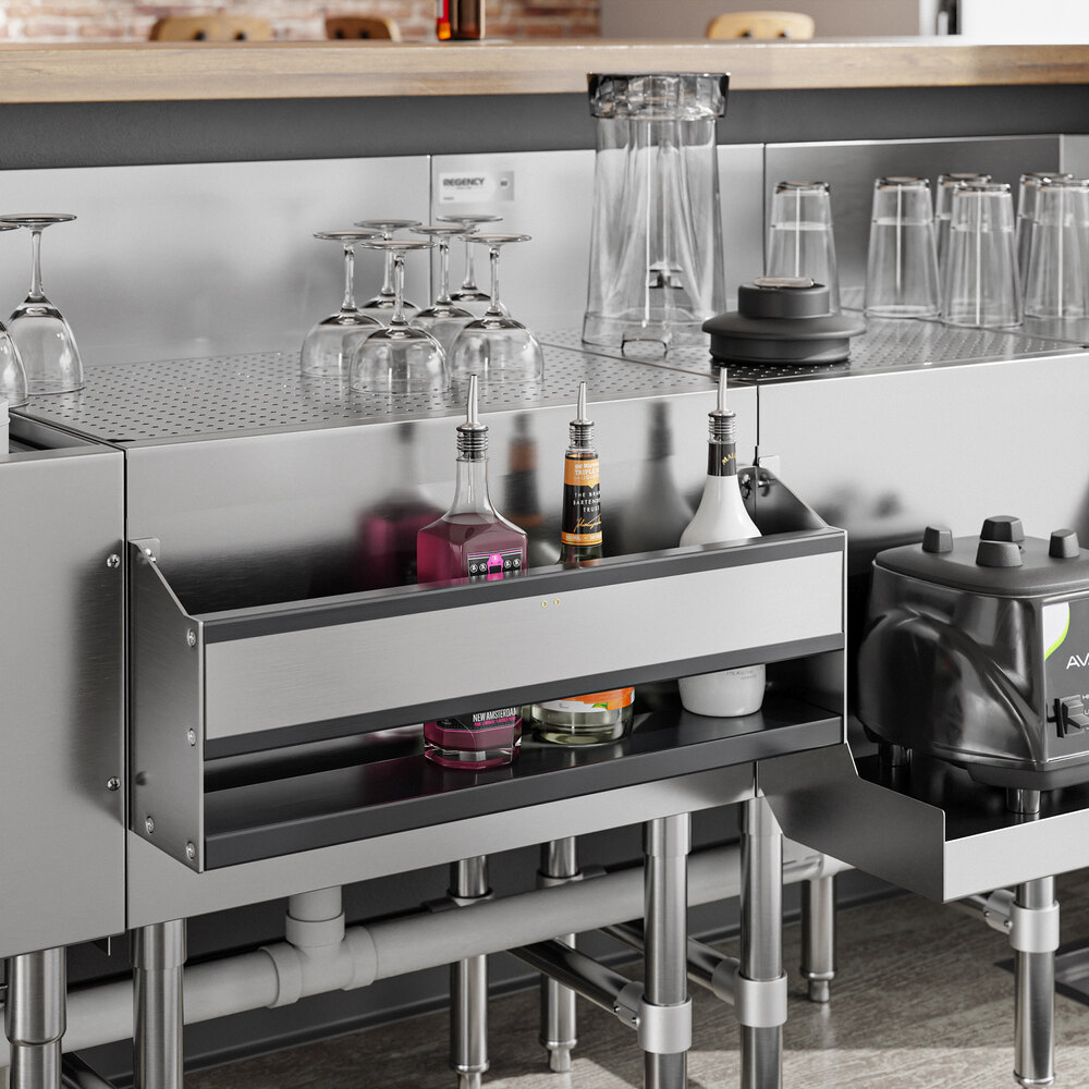 A stainless steel bar setup with a single tier speed rail holding bottles, surrounded by glassware and bar equipment.