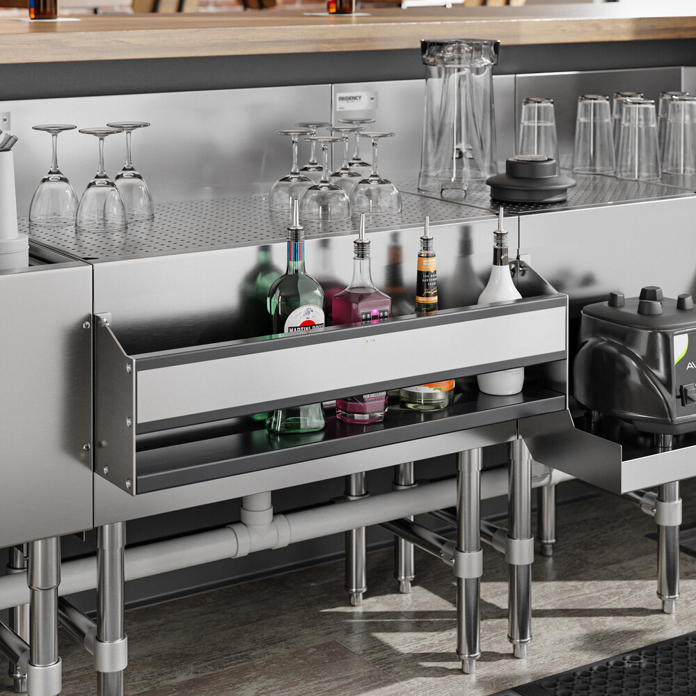A stainless steel single tier speed rail mounted under a bar counter, holding several bottles and bar supplies.