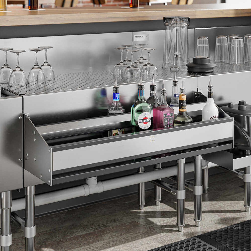 A stainless steel double-tier speed rail filled with various liquor bottles, installed under a bar counter with glassware on top.