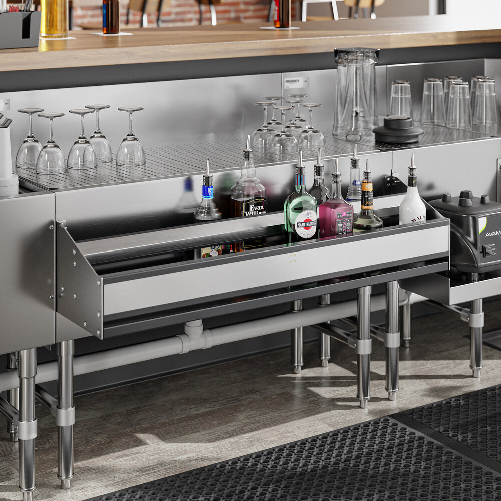 A stainless steel double-tier speed rail mounted under a bar counter, holding various liquor bottles with glassware stored above.