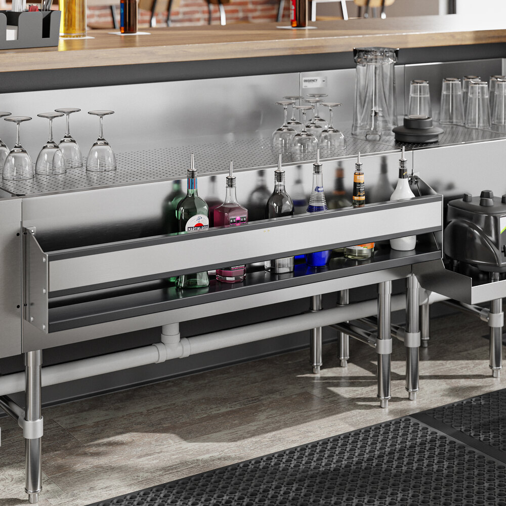 A stainless steel single tier speed rail mounted under a bar counter, holding various bottles of liquor with glassware stored above.