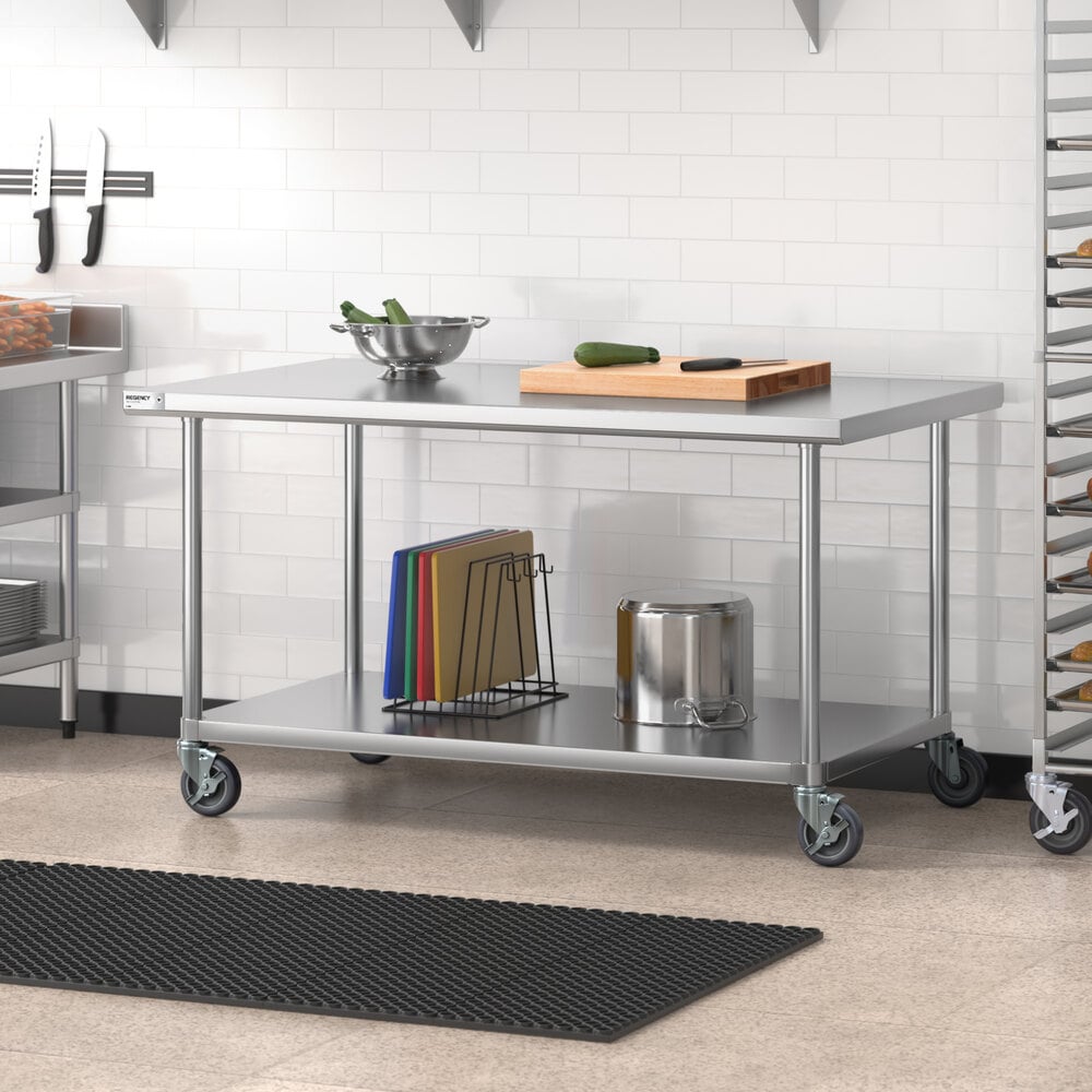 A stainless steel work table with an undershelf and casters, featuring a bowl, cutting board, and knife on top, and cutting boards and a metal container on the lower shelf.