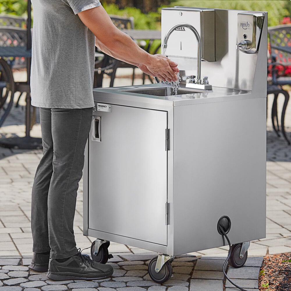 A person is washing their hands at a stainless steel portable hand sink cart with a gooseneck faucet, mounted on wheels.