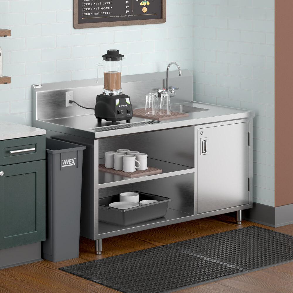 A stainless steel beverage table with a right-side sink, gooseneck faucet, blender, cups, and open shelving, situated in a commercial kitchen setting.