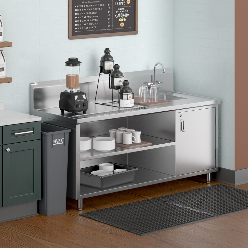 A stainless steel beverage station with a right-side sink, gooseneck faucet, open shelves holding cups and trays, and a blender on the countertop.