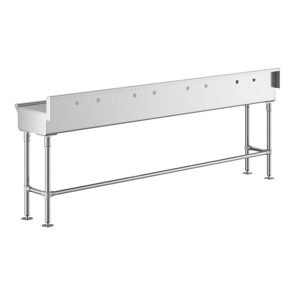 A long, stainless steel hand sink with four sets of faucet holes, supported by metal legs and crossbars.