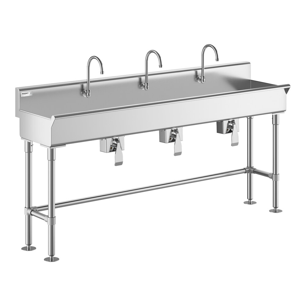 A large stainless steel sink with three gooseneck faucets and knee-operated controls, supported by metal legs.