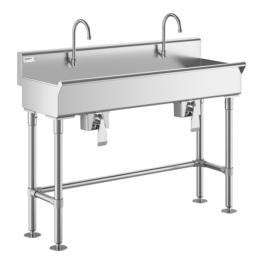 A stainless steel double faucet sink with knee-operated controls and four sturdy legs.