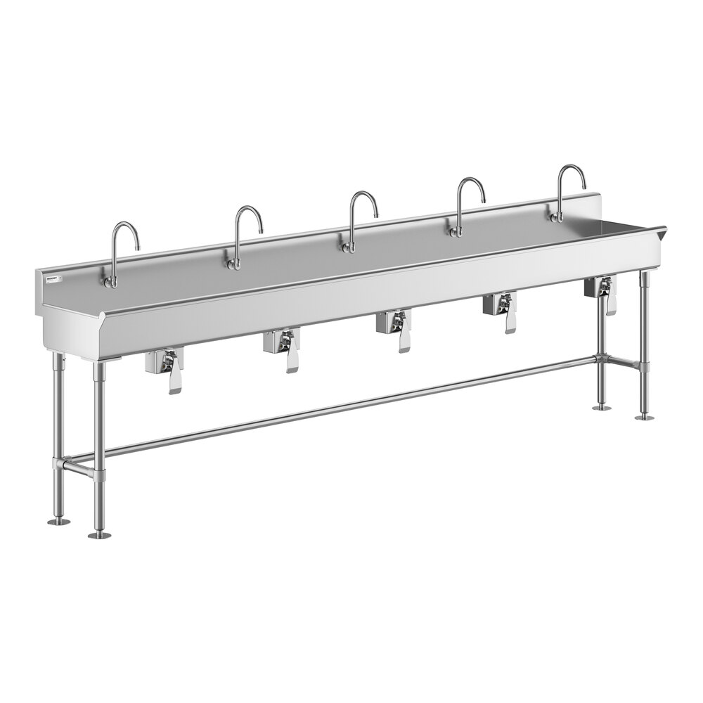 A long stainless steel sink with five knee-operated faucets and sturdy metal legs.