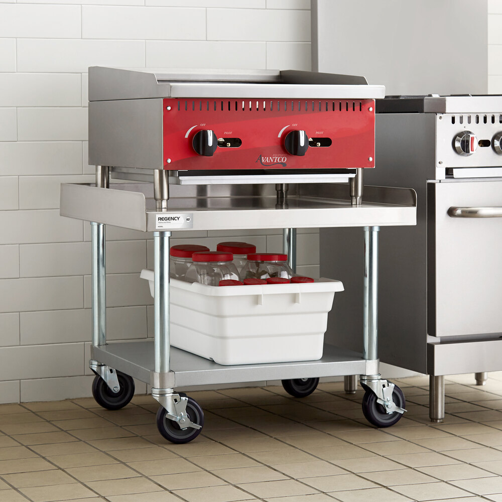 A stainless steel equipment stand with a lower galvanized shelf and four caster wheels, holding a red and silver appliance on top and a white bin with bottles underneath.