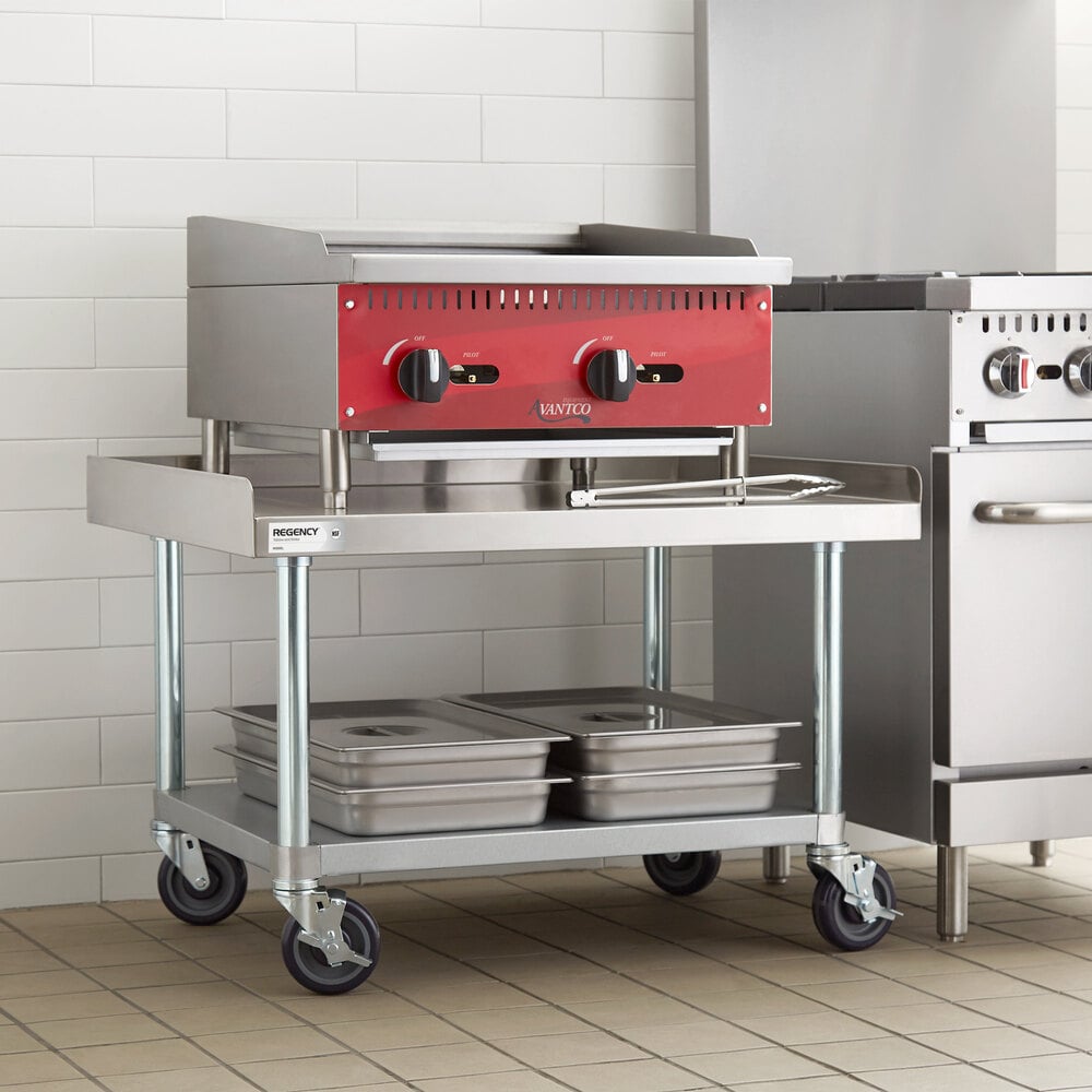A stainless steel equipment stand with a lower galvanized shelf, four caster wheels, and several metal pans stored on the bottom shelf.