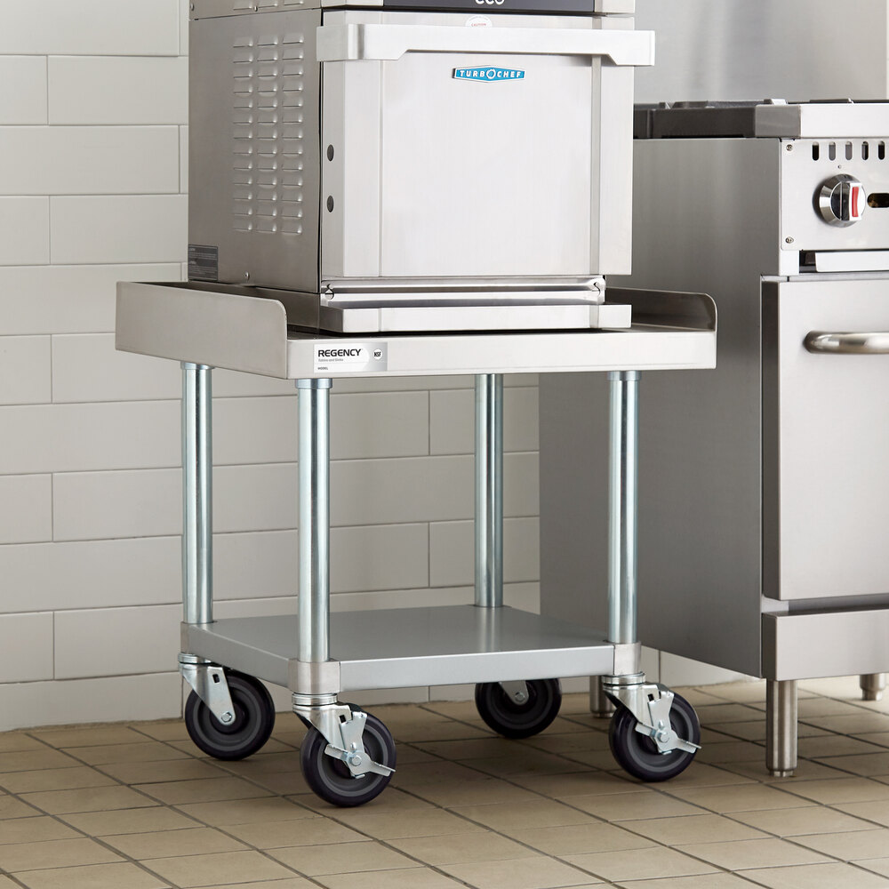 A stainless steel equipment stand with a lower galvanized shelf and four caster wheels, placed in a commercial kitchen setting.