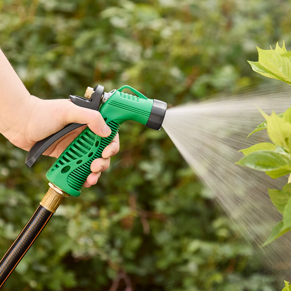 A hand holding a green and black Regency garden spray nozzle spraying a plant.