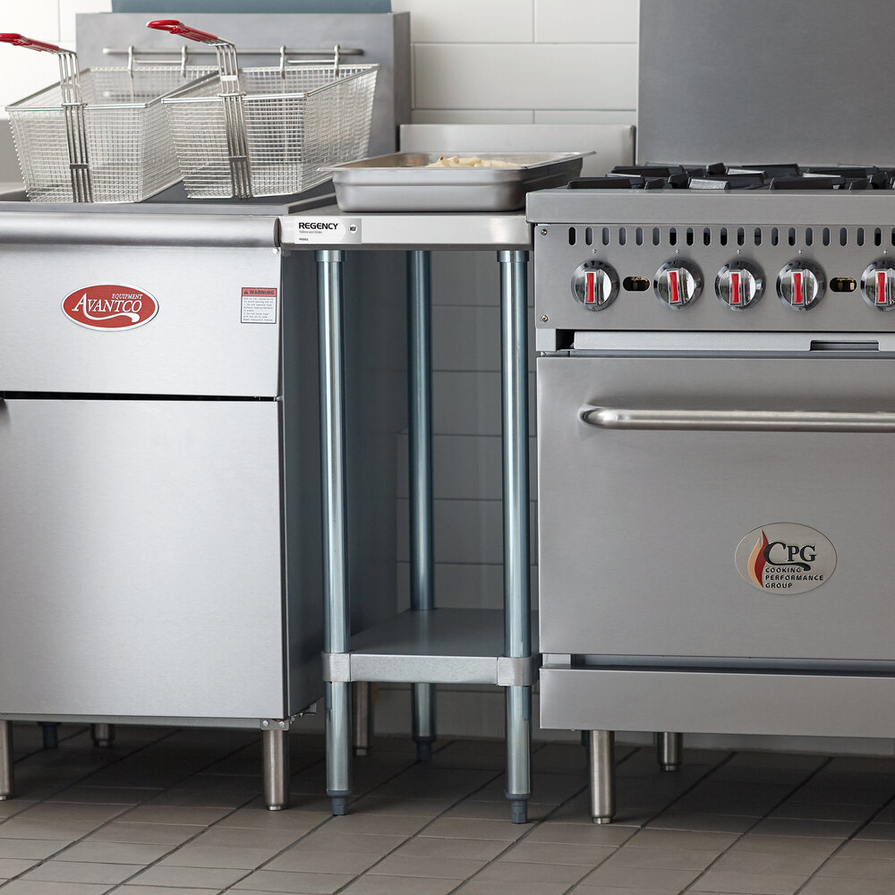 A small stainless steel table with an undershelf is positioned between a fryer and a stove in a commercial kitchen setting.
