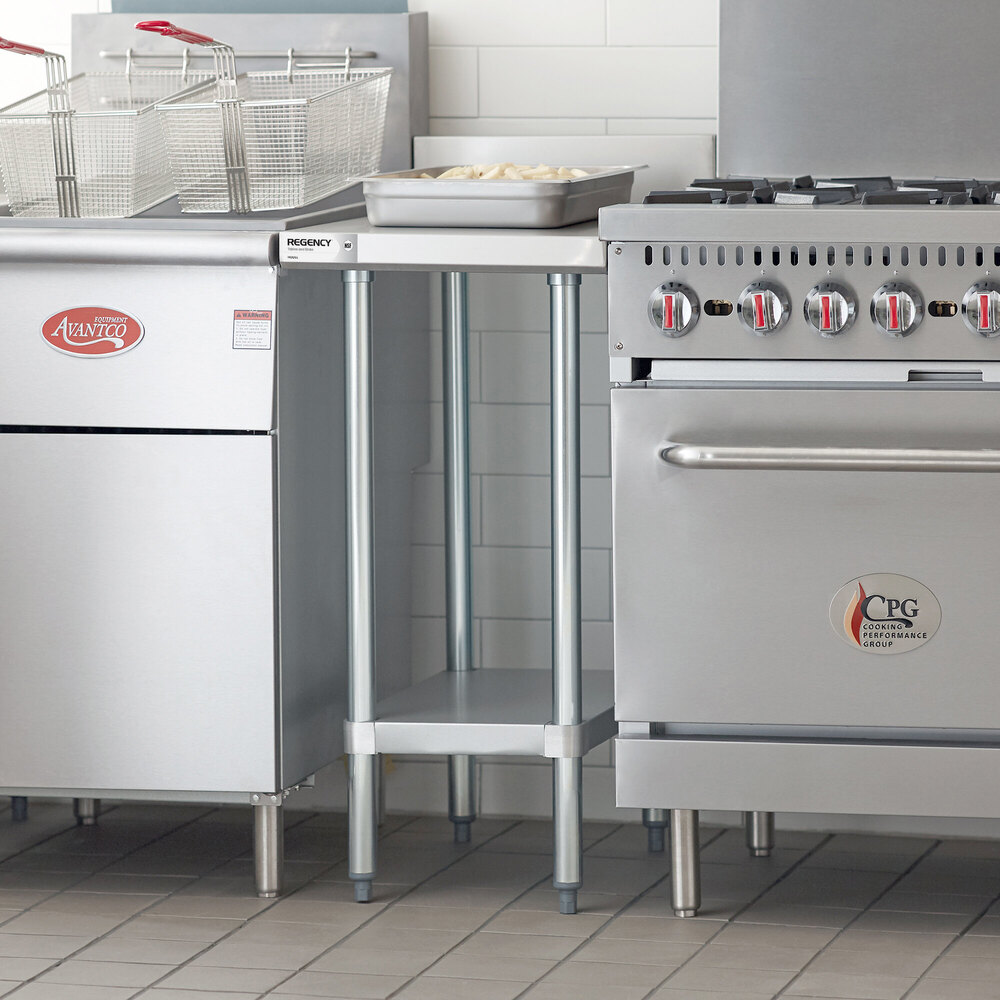 A stainless steel filler table with an undershelf is positioned between a fryer and a range in a commercial kitchen setting.