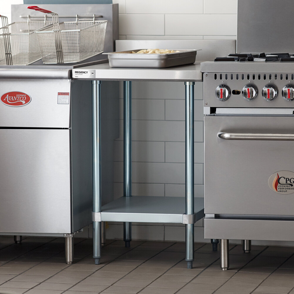 A stainless steel table with an undershelf positioned between a fryer and a stove in a commercial kitchen setting.