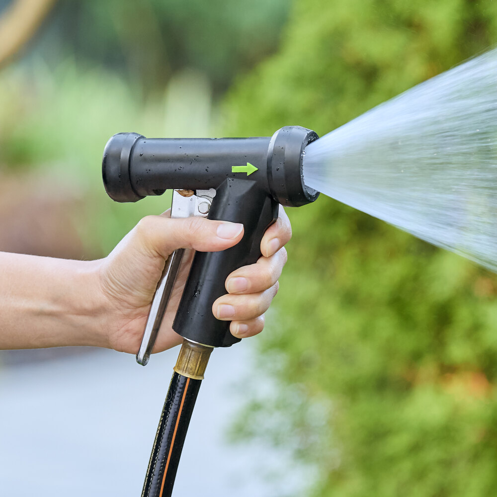 A black brass spray nozzle with a metal handle attached to a hose, spraying water.