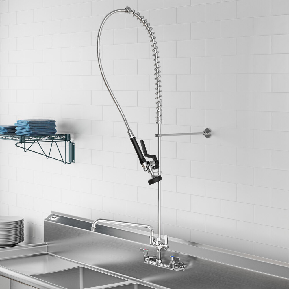 A commercial-style wall-mounted pre-rinse faucet with a flexible hose and spray nozzle, installed above a stainless steel sink in a kitchen setting.